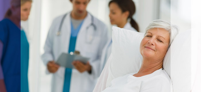 Woman resting comfortably in a hospital bed while Doctors discuss her case behind her.